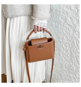 Close-up of a brown handbag with a gold interlocking oval buckle on a grey coat outfit