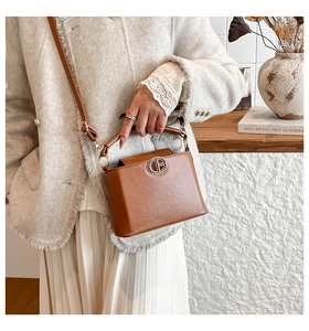 Brown PU leather crossbody bag with silver logo detail shown in an indoor setting