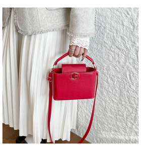 Detail of red square crossbody bag with gold round metal buckle on white textured wall
