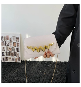 Détail d'une pochette minimaliste en cuir crème avec boucle dorée et bandoulière chaîne