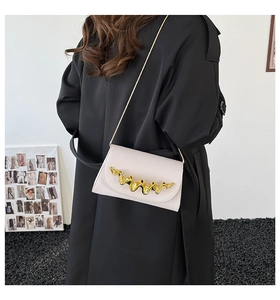 Détail d'un sac bandoulière en cuir beige avec boucle dorée ondulée et fine chaîne
