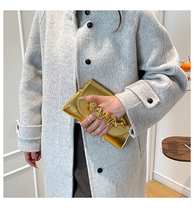 Gros plan détaillé d'une pochette dorée métallique avec poignée ondulée sur manteau