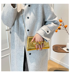 Détail de la poignée dorée sur le sac boîte en acrylique porté avec un long manteau gris