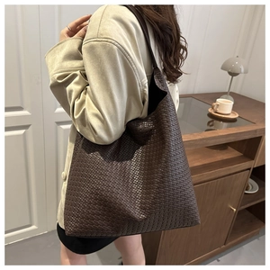 Detailed view of coffee brown woven tote bag worn on shoulder by a model in soft lighting