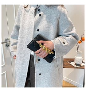 Détail d'un sac à main en cuir noir avec poignée dorée ondulée sur manteau de tweed gris