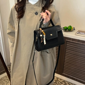 Classic black baguette handbag with gold clasp and wooden bead charm on khaki coat