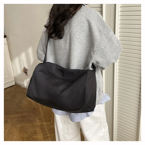 Close-up of a large black nylon travel bag worn by a person in a minimalist interior