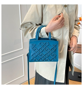 Peacock blue handbag with geometric crown embossing shown on a model