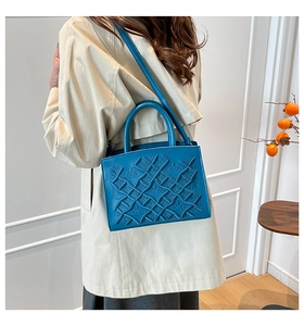 Detailed view of a blue structured handbag with geometric embossing and cross-body strap