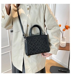 Detail shot of a black embossed lady bag paired with a beige trench coat in a home setting