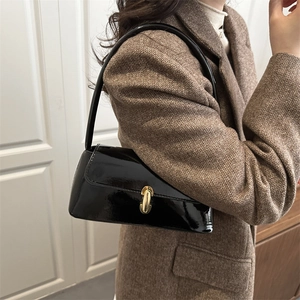 French style black patent leather baguette bag with gold buckle on a brown coat