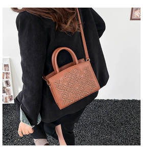 Detailed view of brown patent leather handbag with embossed texture and crossbody strap