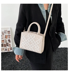Detail of a chic cream crossbody bag with elegant crown embroidery and top handle