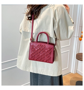 Detail of burgundy patent leather bag with crown relief pattern and adjustable strap