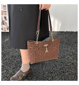 Detail of leopard print tote bag featuring a golden deer charm and chain strap