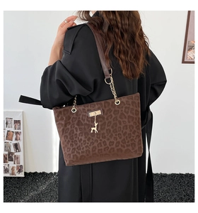 Detail of leopard print tote bag with golden deer pendant and chain strap on shoulder