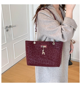 Detail shot of burgundy leopard print tote bag featuring a gold deer charm and chain strap