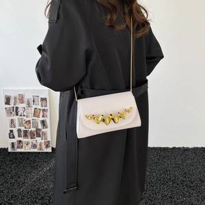 Sac à bandoulière beige en cuir avec boucle dorée ondulée porté par un mannequin