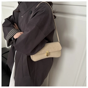 Close-up of beige suede shoulder bag with gold twist lock on dark wool coat