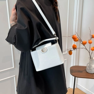 White leather crossbody bucket bag with silver round buckle worn over a black coat