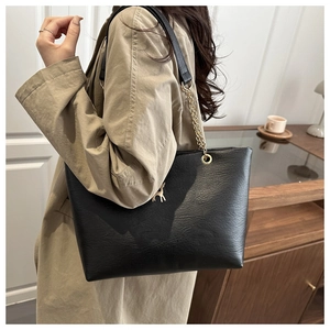 Detailansicht der schwarzen Tote Bag mit goldenem Hirsch-Logo und Kettenriemen am Model