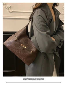 Close-up of woven leather shoulder bag with a gold buckle shown on a model side