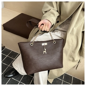 Detail of dark brown tote bag with golden giraffe charm and metal chain handle