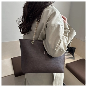 Détail d'un cabas en cuir marron foncé avec chaîne dorée porté sur un manteau beige