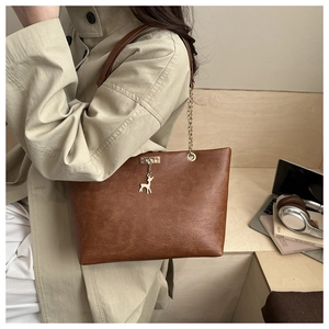 Detail of retro brown tote bag featuring fine texture and golden metal deer charm pendant