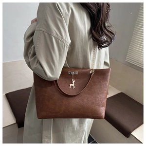 Brown faux leather tote bag detail with gold deer charm and metal chain strap on model