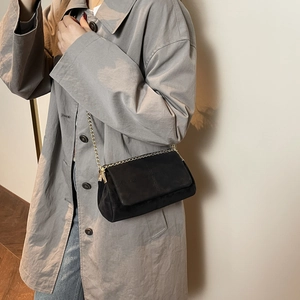Minimalist black quilted crossbody bag with gold chain strap shown on a model