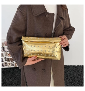 Detail of gold metallic envelope clutch bag featuring silver punk rivets held by a model