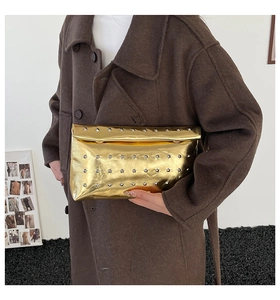 Gros plan d'une pochette enveloppe dorée avec rivets argentés portée sur un manteau