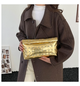 Close-up of golden metallic clutch bag with silver rivets held against a brown coat