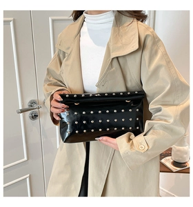 Detail of a black patent leather clutch with silver studs held by a model in a trench coat