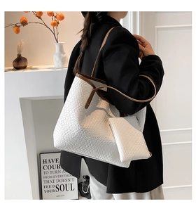 Detail view of woven white tote bag with brown leather straps and matching inner pouch