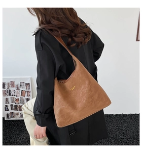 Close-up of brown faux leather shoulder bag with gold lettered branding and soft texture