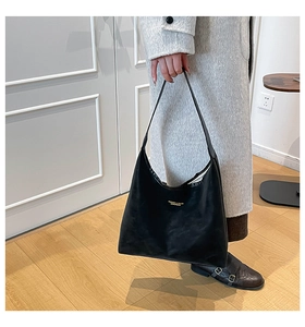 Detail of minimalist black leather tote bag featuring gold lettering and long slim handles