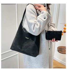 Détail d'un ensemble cabas noir mat et pochette avec logo doré sur manteau gris