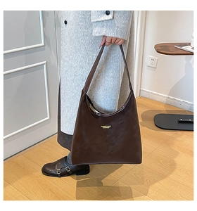 Détail du sac cabas en cuir marron foncé avec lettrage doré tenu par un mannequin