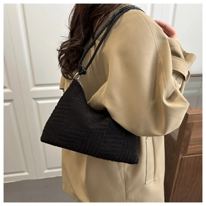 Gros plan sur un sac porté épaule noir tissé avec anneaux argentés sur un trench beige