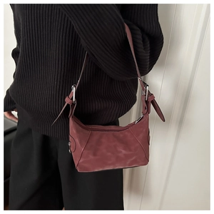 Close-up of burgundy suede shoulder bag with silver buckle detail on a model