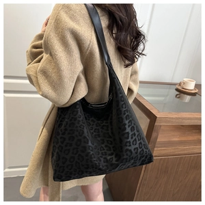 Detail of leopard print tote bag with plush texture and black leather strap on model