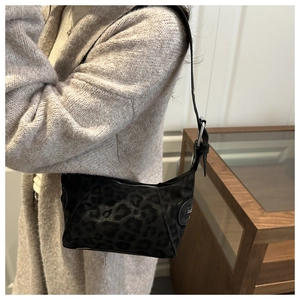 Shoulder bag in black leopard print velvet worn by a model in a warm indoor setting