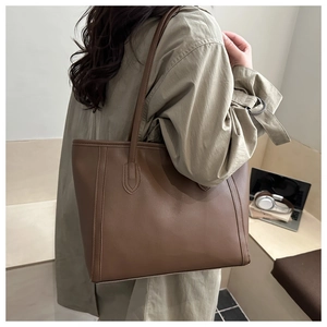 Brown leather tote bag detail with vertical stitching and long shoulder strap for work