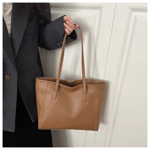 Close-up of brown tote bag with vertical stitching held by model in a blazer