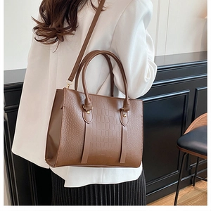 Close-up of brown crocodile pattern tote bag with golden metal hardware on model