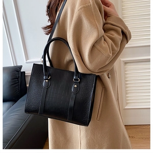 Detail of black faux crocodile pattern tote bag with gold hardware and shoulder strap