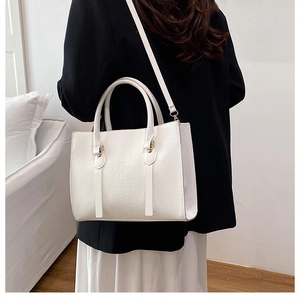 Detailed view of white crocodile pattern tote bag with gold hardware on a model