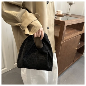 Close-up of black leopard embossed velvet handbag paired with a beige winter coat